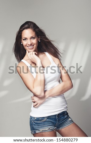 Happy sexy young woman posing in trendy denim shorts and a white summer top smiling at the camera, three quarter portrait