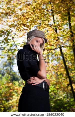 Low angle view of a slender attractive young woman in trendy modern clothes standing in an autumn garden looking down at the camera with a thoughtful expression