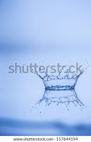 Water explosion with dynamic motion as the drop causes a circular splash with spray suspended above the surface of the water and reflected in the pure liquid below