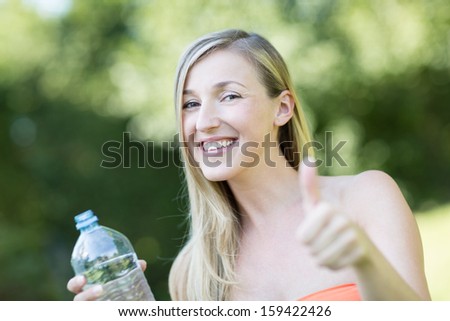 Smiling beautiful woman giving a thumbs up of approval for the bottle of fresh pure water that she is holding endorsing it as the thirst quencher of choice
