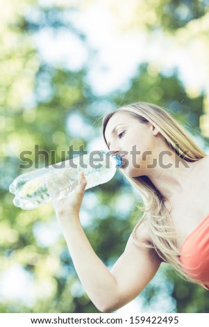 Low angle view of a thirsty young woman drinking refreshing bottled water while enjoying a hot summer day in nature