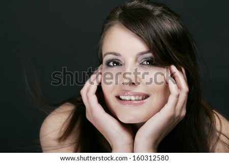Portrait of a beautiful smiling woman leaning forward and holding her head in her hands with a captivated expression