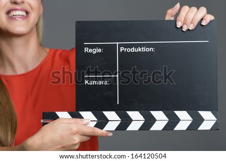 Smiling woman holding a clapperboard during a film production to give the sound to commence recording of the audio during each new take