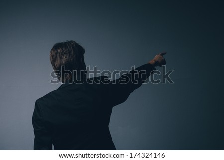 Businessman in a stylish suit standing with his back to the camera pointing ahead and calling your attention towards copy space on a grey background
