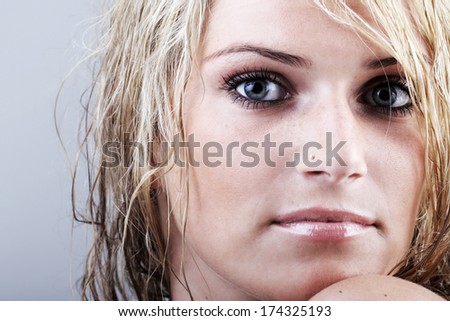 Beautiful blond woman with tousled damp hair and a sombre enigmatic gaze staring intently at the camera, close up view of her face