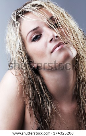Seductive beautiful young blond woman with long wet hair and naked shoulders tilting her head back and looking languidly at the camera, close up of her head and shoulders
