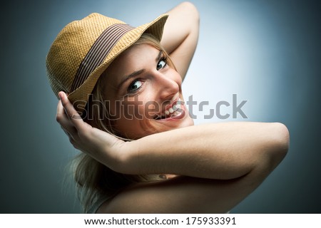 Laughing charismatic young woman wearing a trendy straw hat turning to look back at the camera with a beautiful smile