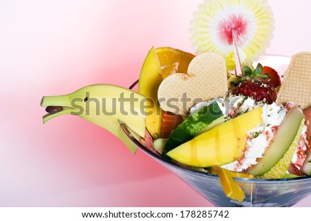 Tropical fruit salad and ice cream garnished with a decorative banana cut to resemble a birds head and served in a cocktail glass