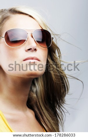 Glamorous blond woman in sunglasses with her hair blowing in the breeze staring off thoughtfully into the distance with a serious expression