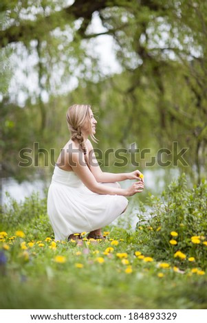Side view of a beautiful dreamy young woman relaxing in nature sitting in a field of dandelions alongside a lake staring off into the distance in meditation