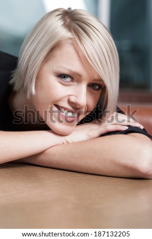 Smiling happy contented young woman with a short blond hairstyle resting her chin on her crossed arms with a look of pleasure