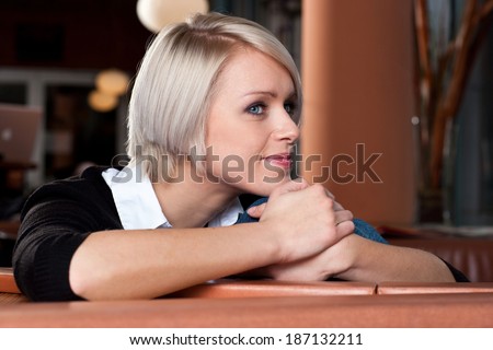 Beautiful young woman smiling in contentment and glancing sideways at the camera as she rests her chin on her hands on a counter at the bar