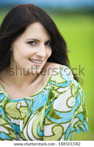 Beautiful natural woman with a beaming smile, closeup head and shoulders portrait against a blurred green grassy background