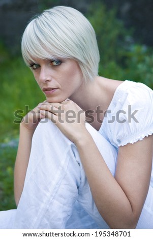 Beautiful serene young blond woman sitting enjoying the freedom of nature resting her chin on her knee looking sideways at the camera with a calm expression