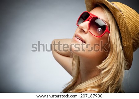 Close up profile portrait of the face of a beautiful elegant tanned blond woman in trendy sunglasses and a hat, on grey with copy space and a vignette
