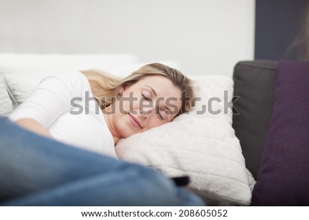 Exhausted attractive young woman taking a nap on the sofa lying curled up with her eyes closed and a lovely smile as she dreams pleasant dreams