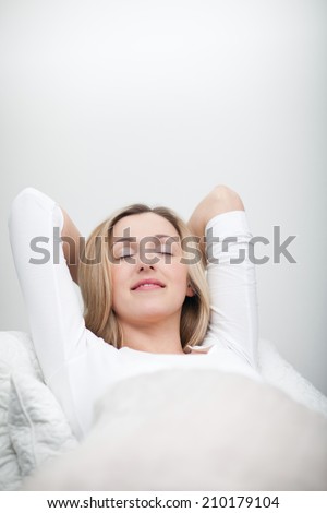 Blissful young woman relaxing in bed stretched out on her back with her hands behind her head and a beautiful smile of satisfaction