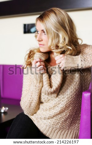 Beautiful blond woman in a bar or cafeteria wearing a stylish winter polo neck staring off thoughtfully to the side watching something