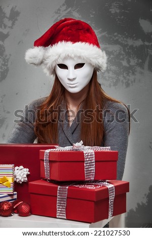 Woman in White Mask and Santa Clause Hat with Red Gift Boxes in Front.