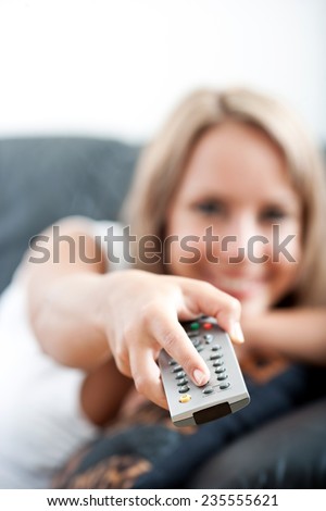 Young woman watching television with a remote control aimed at the screen to change the program or channel, focus to the remote and her hand