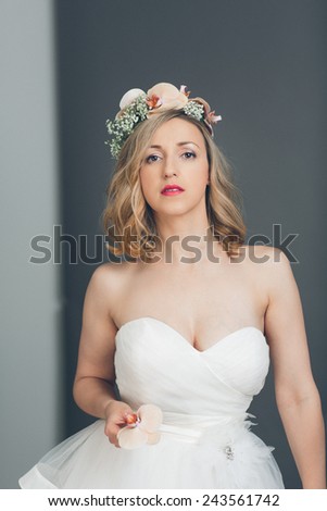 Elegant sophisticated young blond bride in a strapless white wedding dress with flowers in her hair standing looking at the camera with a serious expression