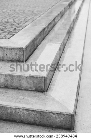 Corner angle of three exterior concrete urban steps with cobblestones above in a street or courtyard with the point of the corner facing the camera in an architectural background