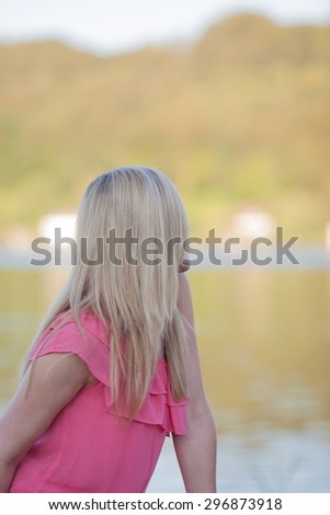 Thoughtful Blond Young Woman in Pink Dress Relaxing at the Lakeside and Looking Into the Distance.
