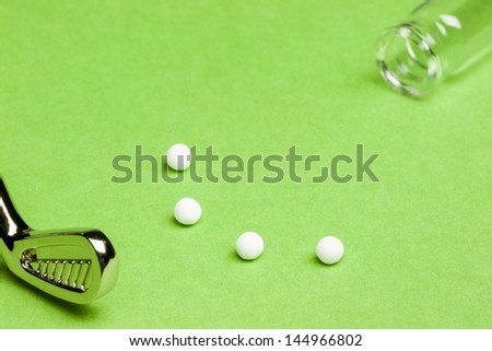 Fun with Homeopathy - A concept suggesting homeopathy as alternative medicine is fun. A mini golf club is used to putt the pills into the mouth of the bottle. The image has a shallow Depth-of-Field.