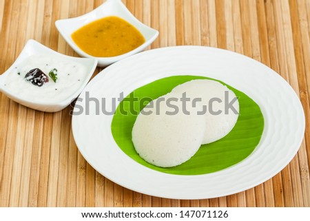 Idly with Chutney, Sambar - A traditional ethnic south Indian breakfast of Idly (Idli / rice cake) served with coconut chutney and sambar on a plate lined with banana leaf.
