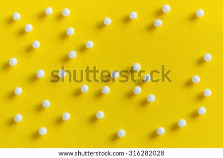Homeopathic pills scattered - Overhead view of homeopathic pills (made from inert substance - sugar/lactose) scattered on a yellow surface. Natural light used.