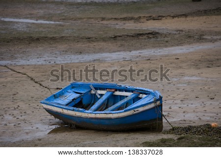 Little boat at low tide. Blue old boat stranded on beach at low tide. Asturias, North Spain.