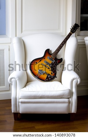 Vintage traditional semi-hollow electric guitar with f-holes on a white  armchair. Electric Guitar on an Armchair.