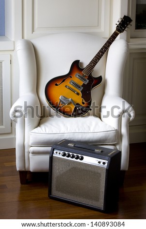 White armchair with an electric guitar and his amplifier. Electric Guitar and Amplifier .