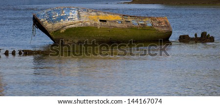 Panoramic view of the hull of an old blue wooden boat stranded and emerging from the surface. Abandoned blue boat.