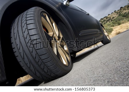 Close view of the wheel of a black sport car with the asphalt at foreground. Wheel.