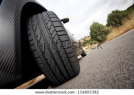 Close view of the wheel of a black sport car with the asphalt at foreground. Tire.