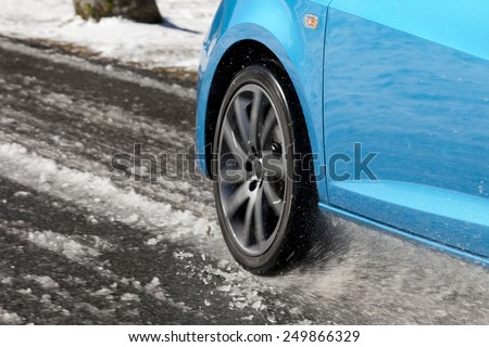 Detail of a car tire driving and splashing on the snow.  Driving on a snowy road