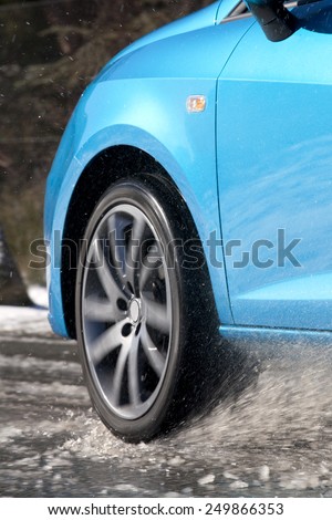 Vertical view of a car tire driving and splashing on the snow.  Driving on a snowy road.