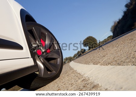 View of the wheel of a withe sport car on a road with blue sky on the background. \
Wheel on a road
