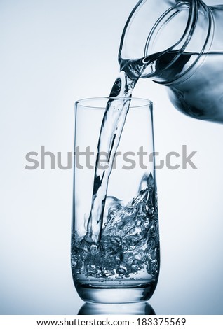 Pouring water from glass pitcher on blue background