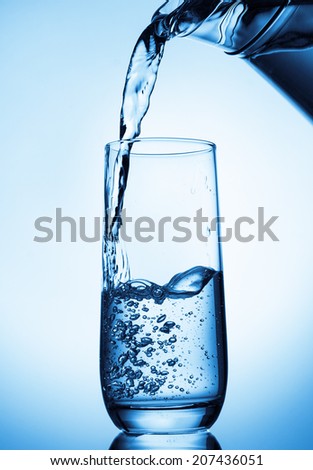 Pouring water from glass pitcher on blue background