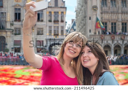 women taking a self portrait with smartphone against flower carpet in Grand Place, Brussels, Belgium