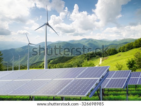 solar panels with wind turbines against mountanis landscape against blue sky with clouds
