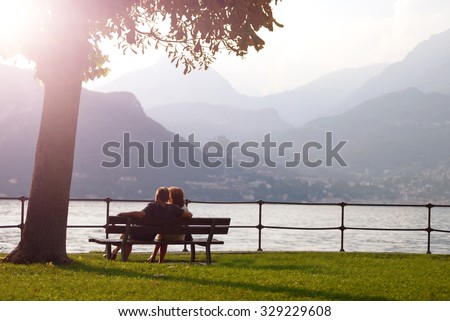 aged couple sitting on a bench under a tree and looking at sunset at Como lake, Bellagio, Italy