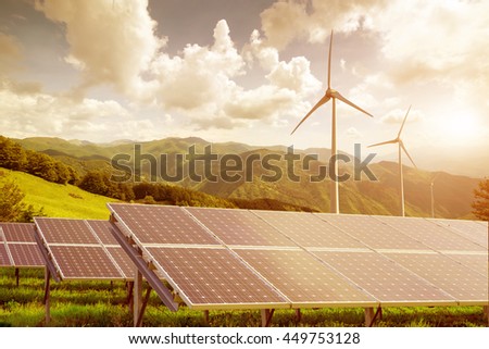 solar panels with wind turbines against mountains landscape against blue sky with clouds on sunset