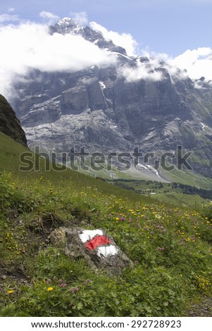 Sign indicating an hiking trail with red and white paint on a rock. Landscape in the Swiss Alps, Berner Oberland, Switzerland.