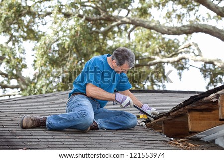 Man using crowbar to remove rotten wood from leaky roof. After removing fascia boards he has discovered that the leak has extended into the beams and decking.