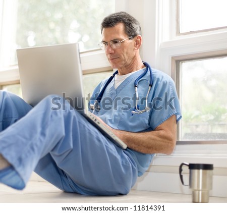 Doctor in blue scrubs relaxing with his laptop on coffee break. Selective focus.