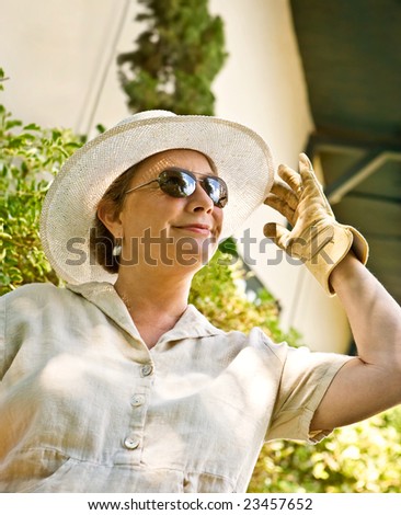 Mature, senior woman in sunhat and gardening gloves greeting the sunny day with enthusiasm