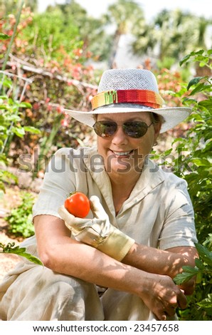 Mature, senior woman in her backyard garden, holding the first tomato of the season.